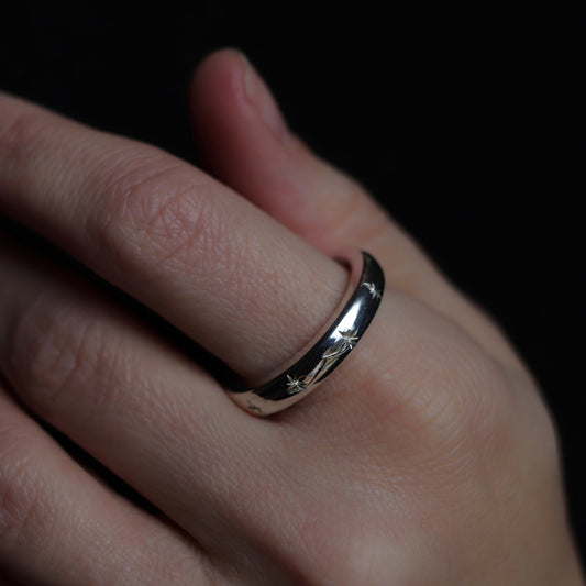 Close-up of a hand wearing a silver ring with a dark background