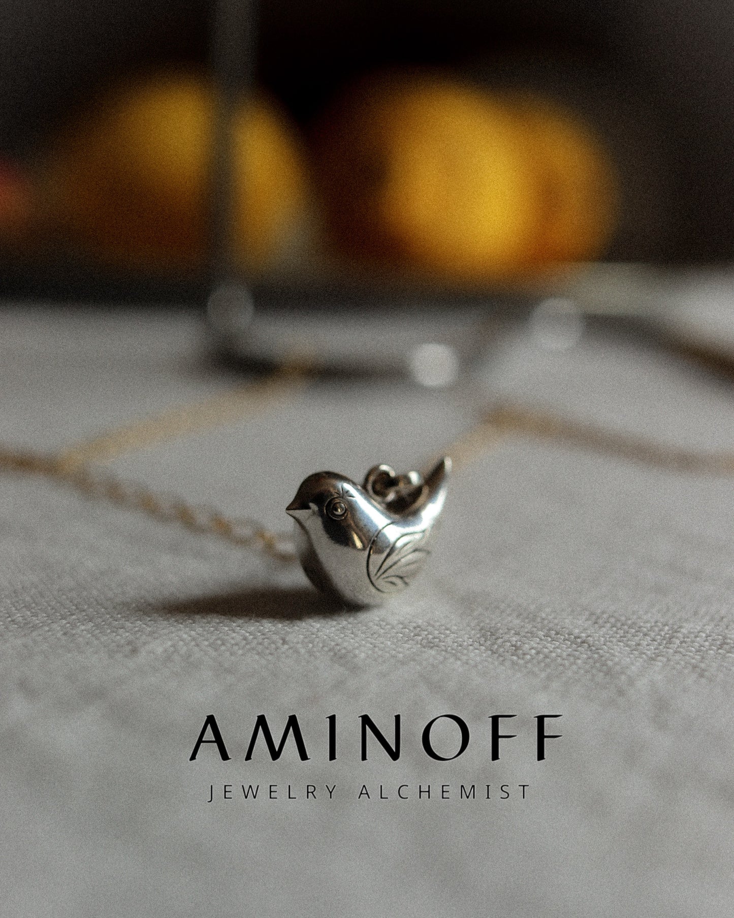 Silver bird-shaped pendant on a chain with 'Aminoff' branding on a textured surface.