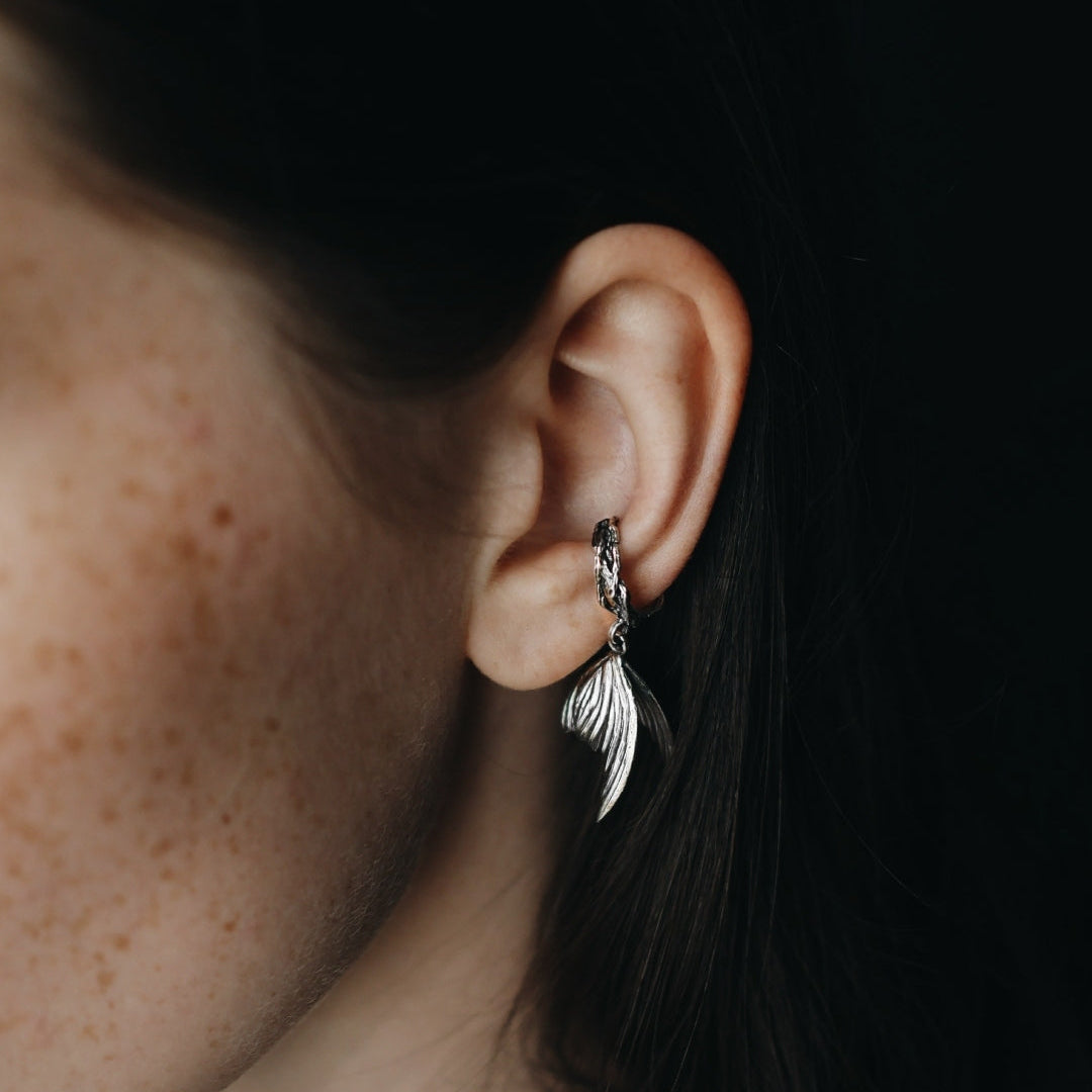 Close-up of an ear wearing a silver feather earring against a dark background