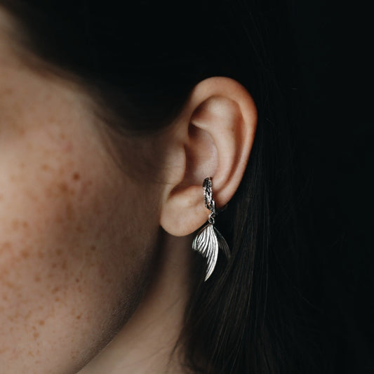 Close-up of an ear wearing a silver feather earring against a dark background