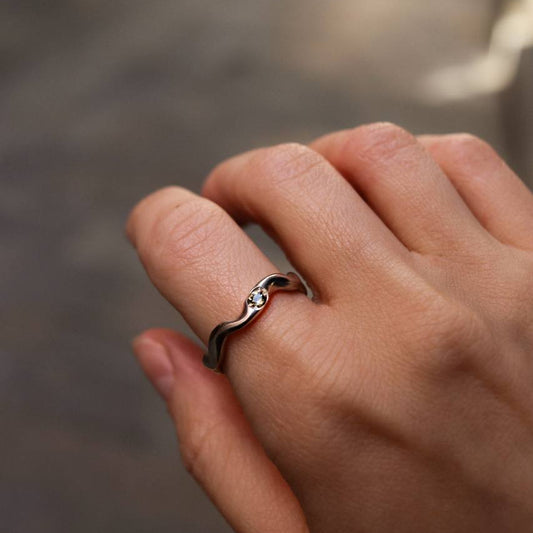 Hand wearing a silver ring with a wavy design on a blurred background