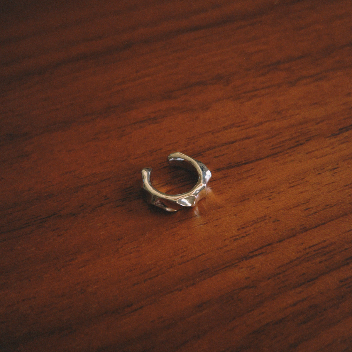 A small silver-toned ring with a textured, organic leaf-like pattern, resting on a dark brown wooden surface.