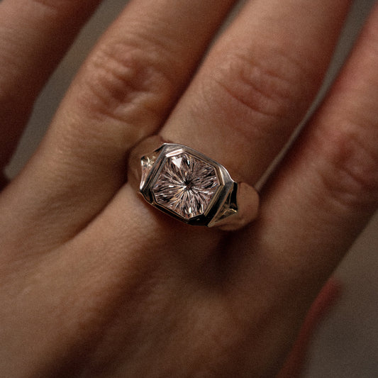Close-up of a hand wearing a ring with a large diamond on a neutral background