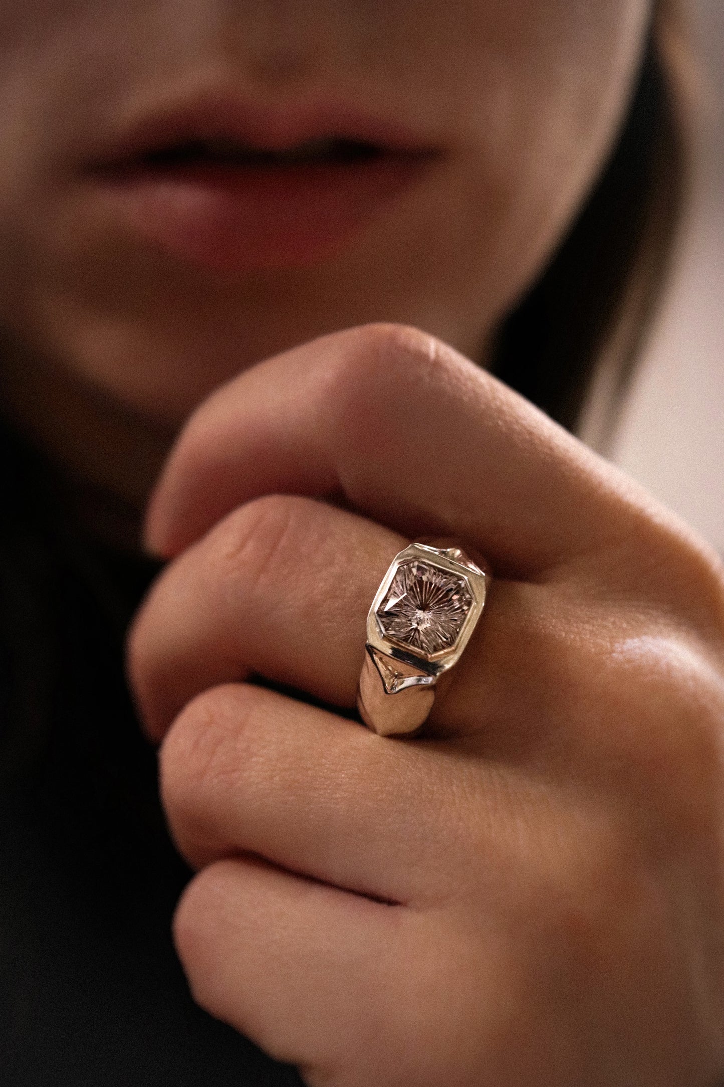 Close-up of a hand wearing a gold ring with a diamond on a blurred background