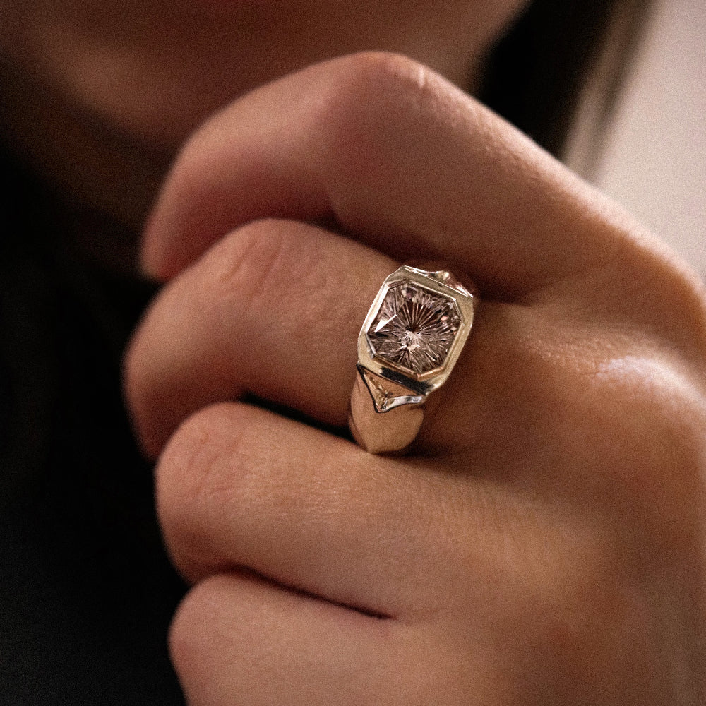 Close-up of a hand wearing a gold ring with a diamond on a blurred background