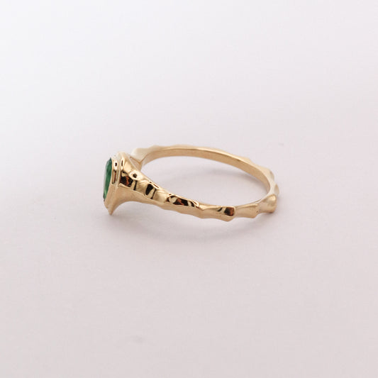Gold ring with a green gemstone on a light gray background