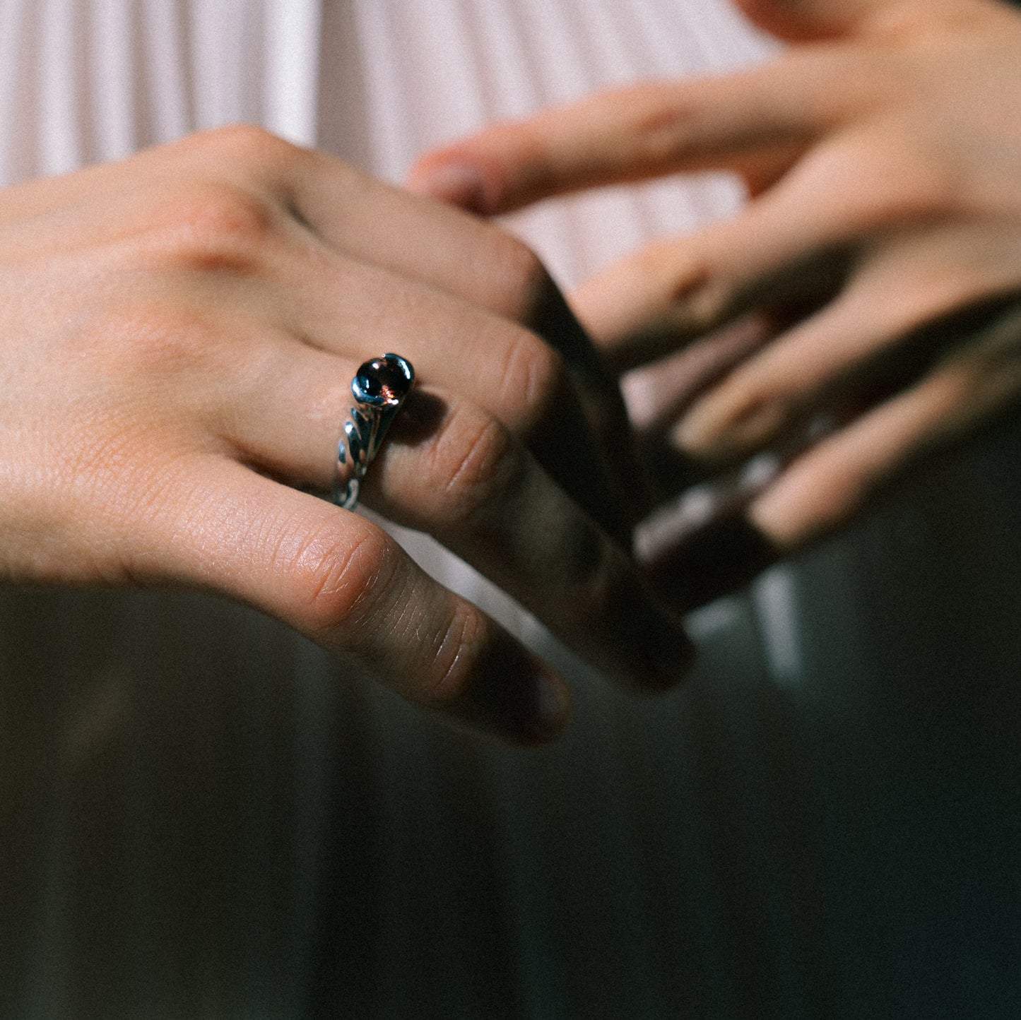 Close-up of a hand wearing a ring with a blue gemstone, against a blurred background.