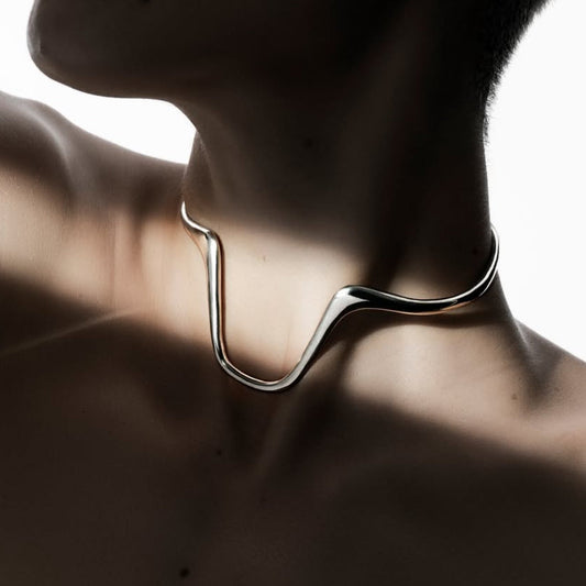 Close-up of a person wearing a modern silver necklace against a blurred background