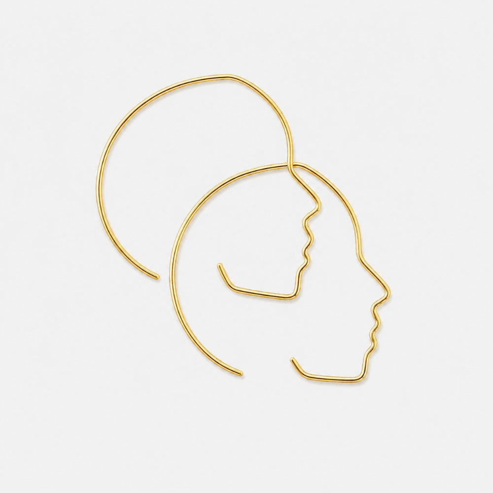 Gold profile-shaped earrings on a light gray background