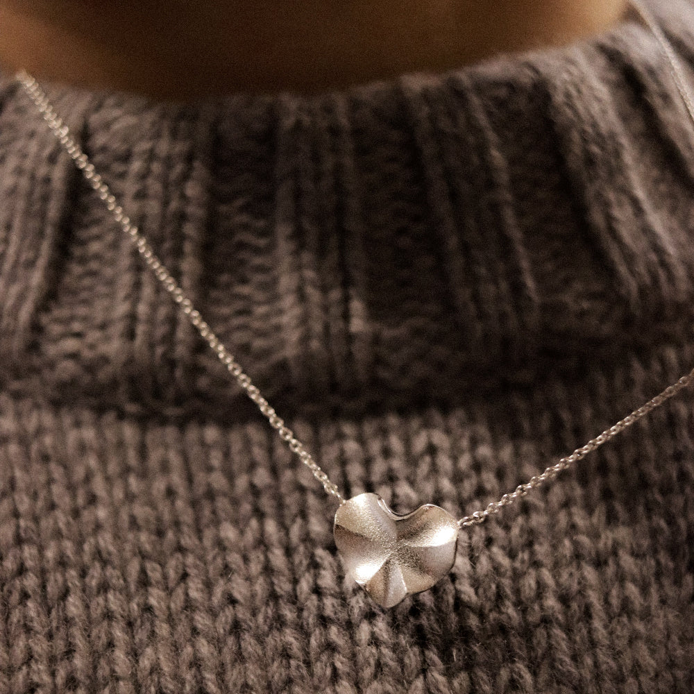 Silver four-leaf clover necklace on a brown knitted sweater