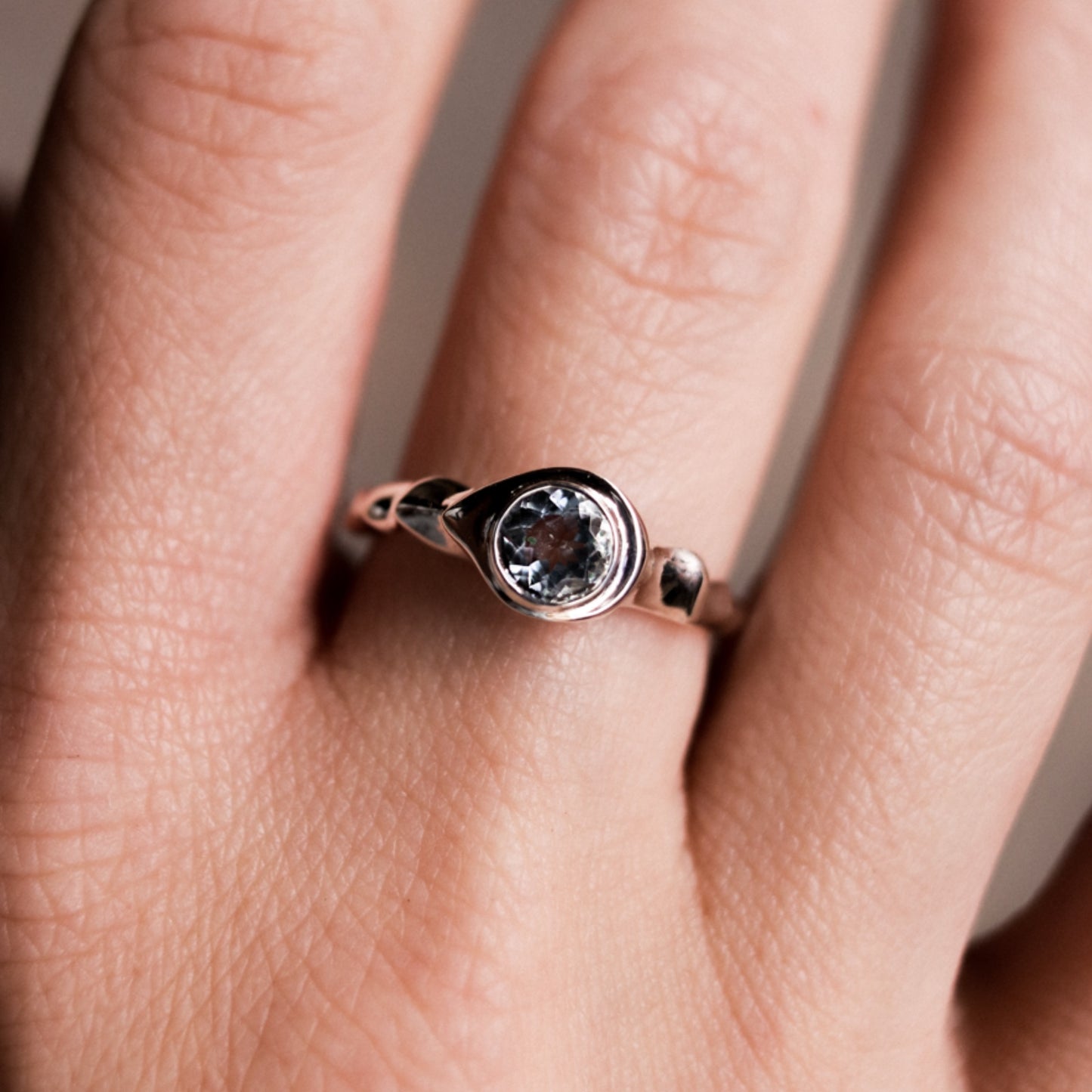 Rose gold ring with a central gemstone on a person's finger against a neutral background