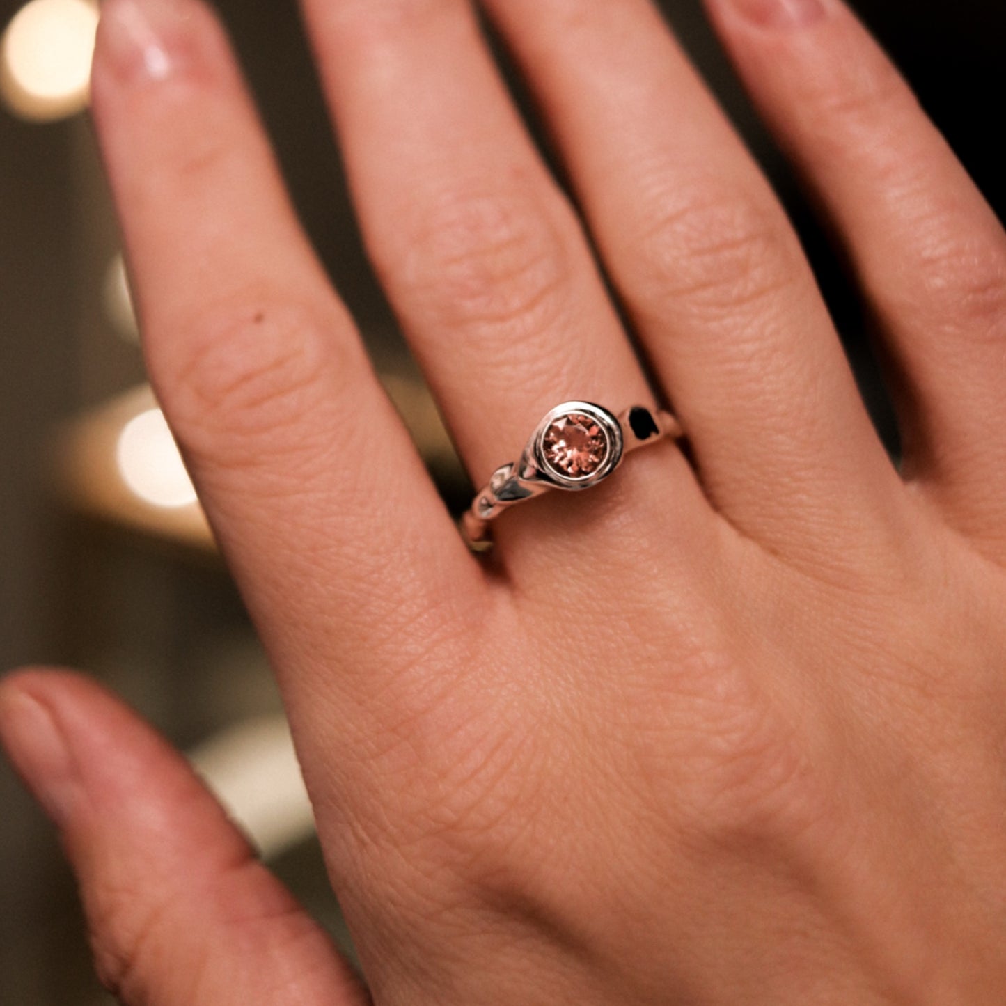 Close-up of a hand wearing a ring with a brown gemstone on a blurred background