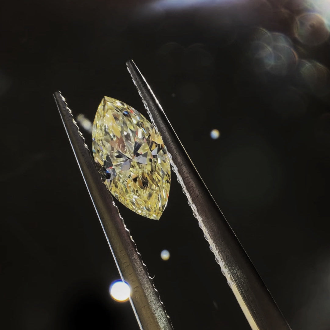 A marquise-cut yellow diamond held between metal tweezers against a dark, softly lit background.
