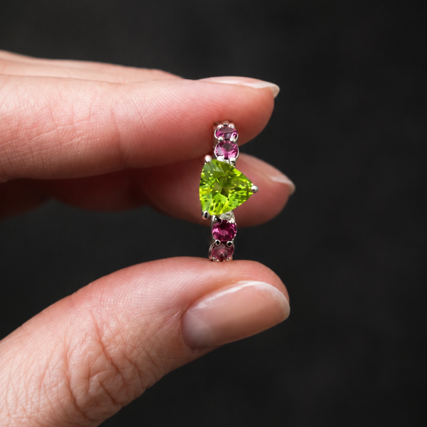 Jewelry with green gemstone held between fingers against a dark background