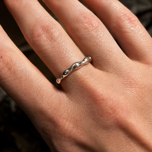 Close-up of a hand wearing a delicate silver ring with a wavy design.