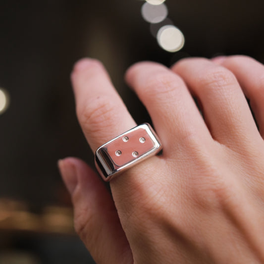 Silver ring with three small stones on a person's finger against a blurred background