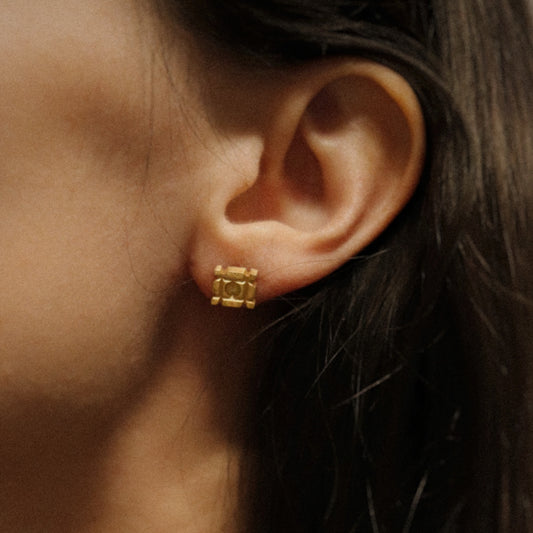 Close-up of an ear wearing a gold earring with a neutral background