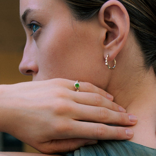 Close-up of a woman wearing earrings and rings with another person's hand on her shoulder.