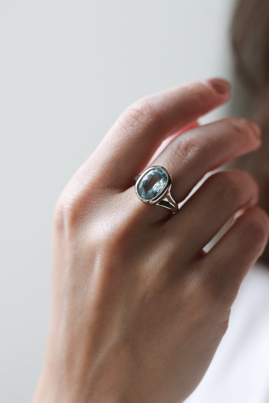 Hand wearing a ring with a blue gemstone on a neutral background