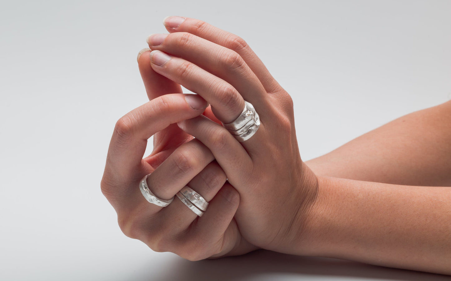 Close-up of hands wearing silver rings on a light gray background