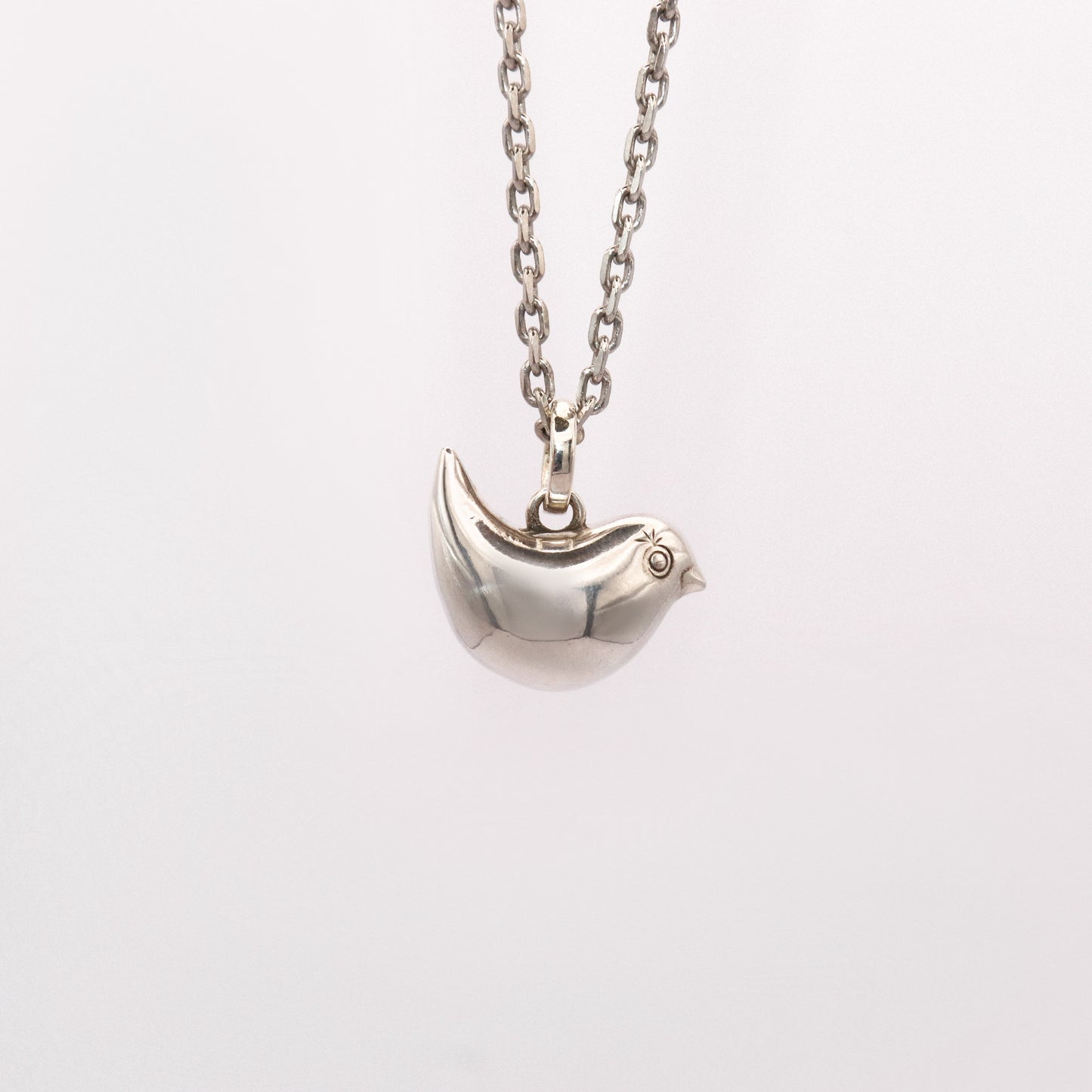 Silver bird-shaped pendant on a chain against a white background