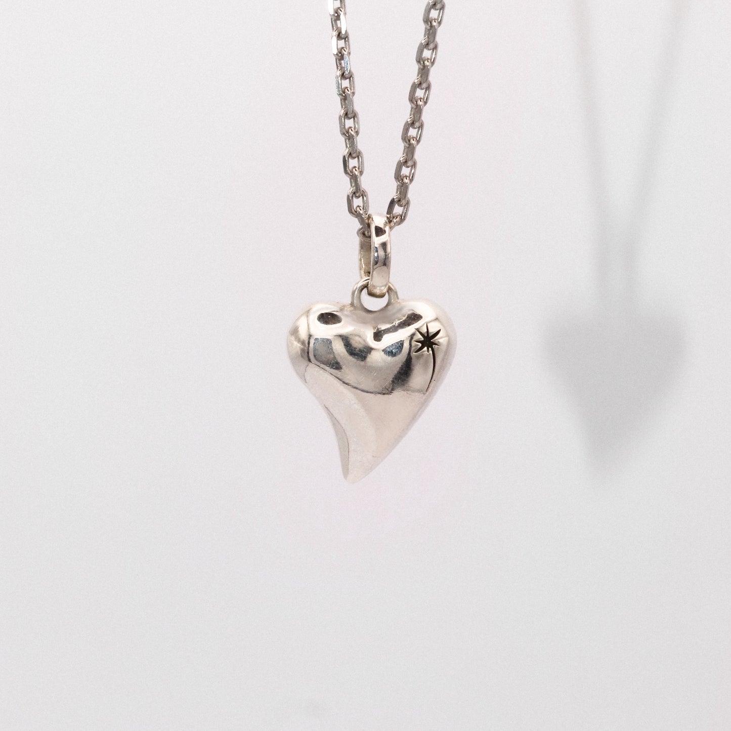 Silver heart-shaped pendant on a chain against a light gray background