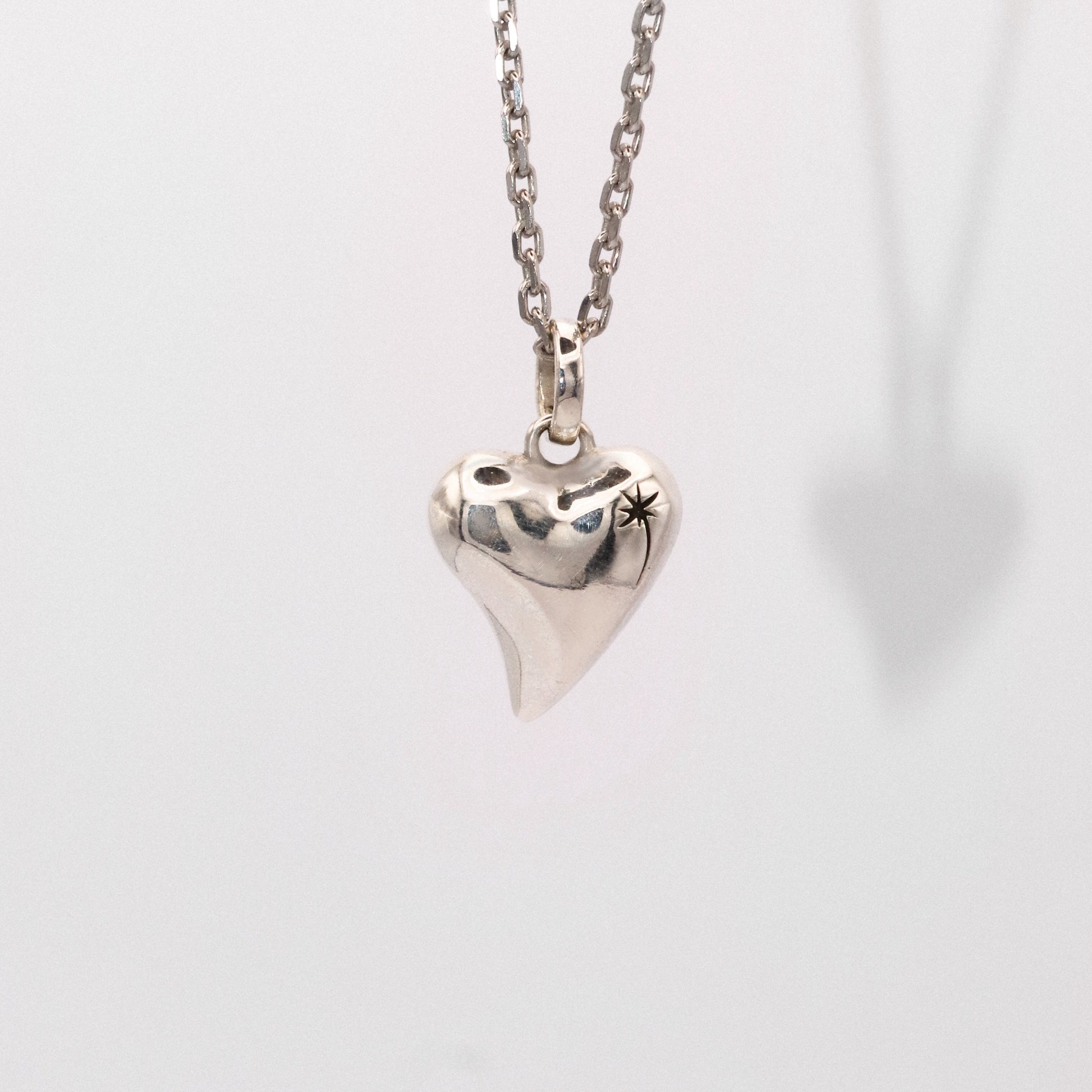 Silver heart-shaped pendant on a chain against a light gray background