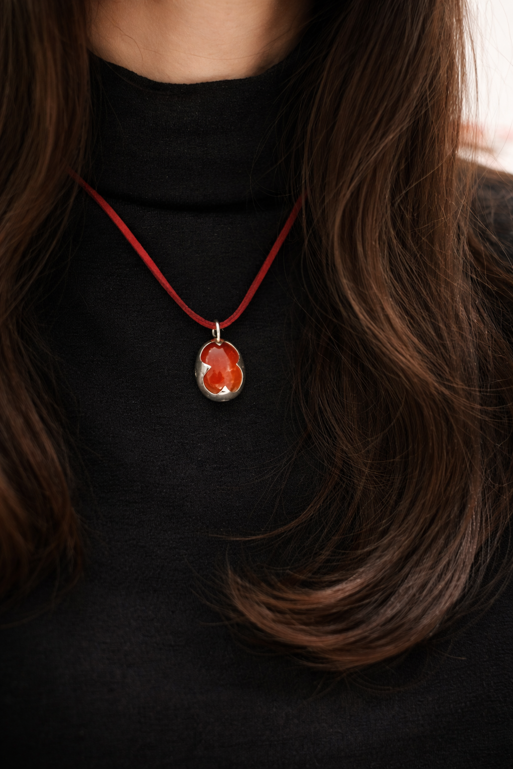 Person wearing a black turtleneck with a red necklace featuring an orange pendant.