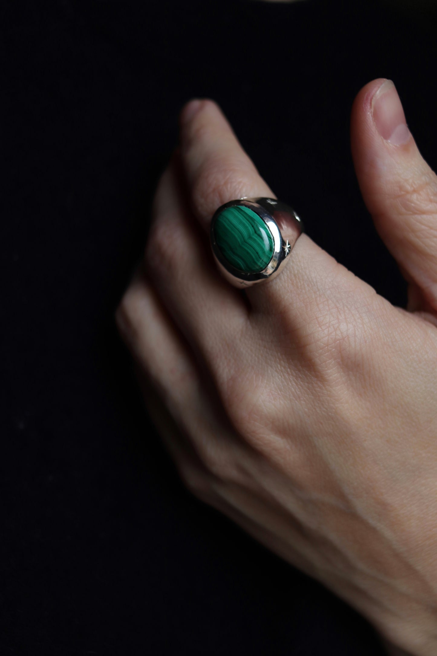 Hand wearing a ring with a green gemstone on a dark background