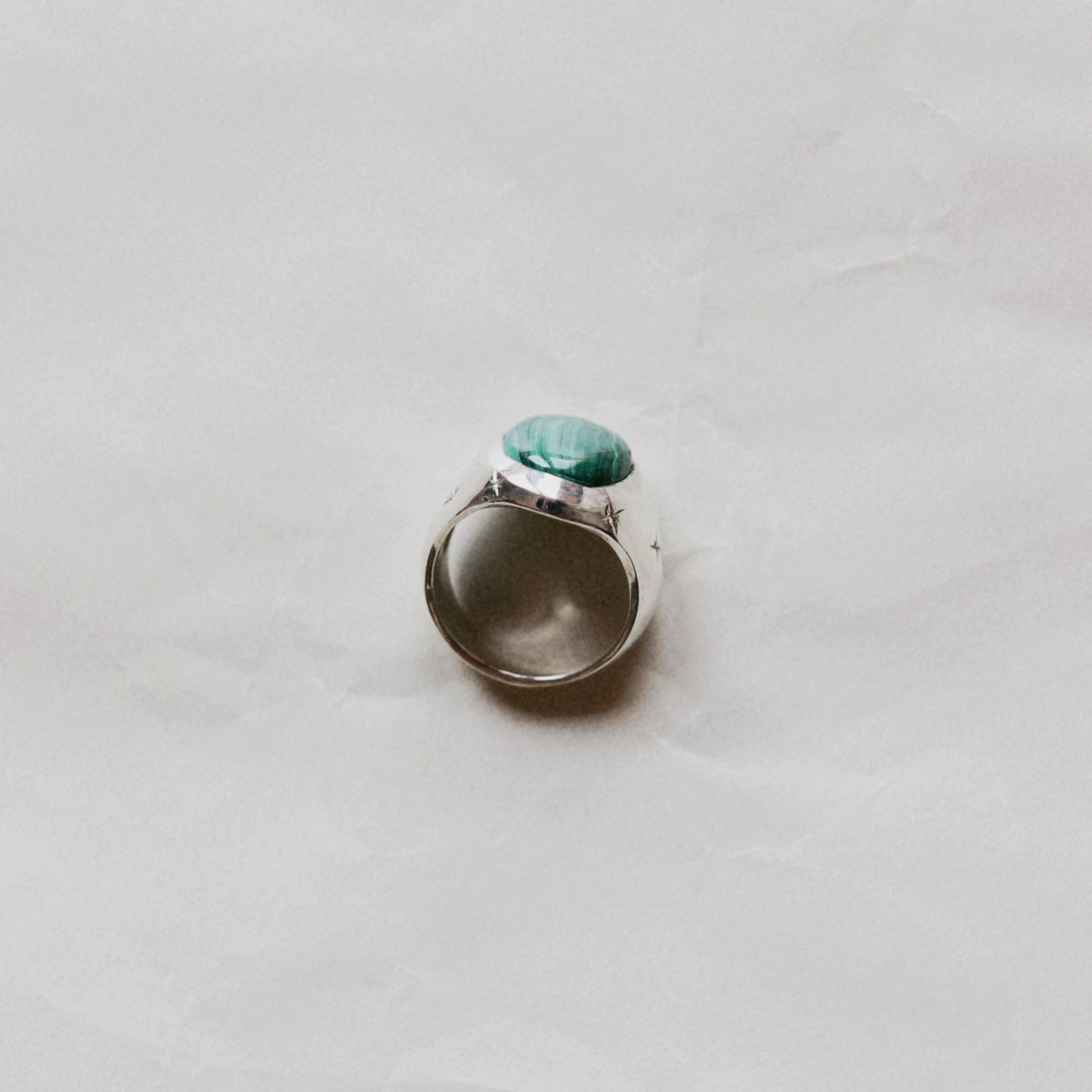 A silver ring with a round green stone, photographed from above on a light gray textured surface.