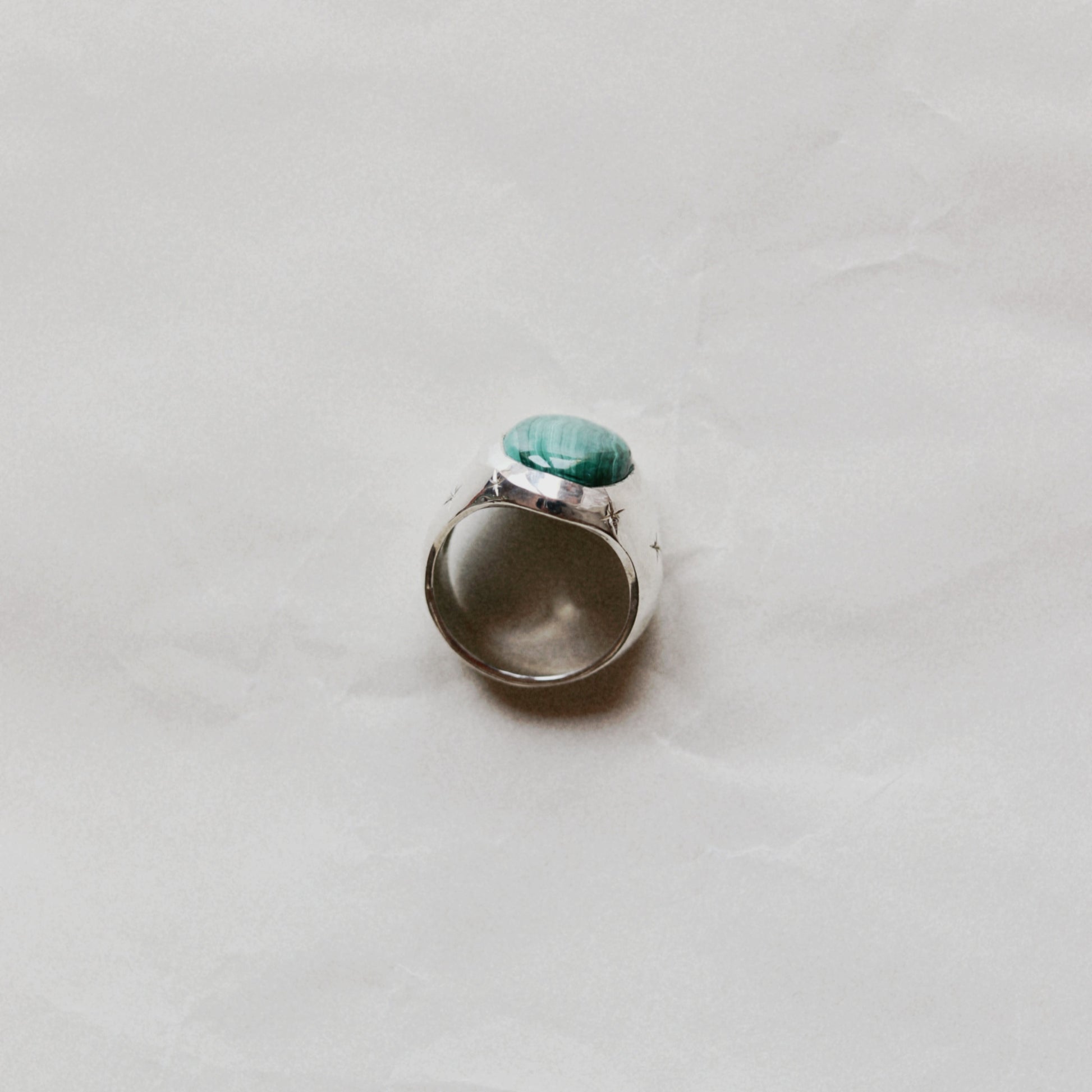 A silver ring with a round green stone, photographed from above on a light gray textured surface.