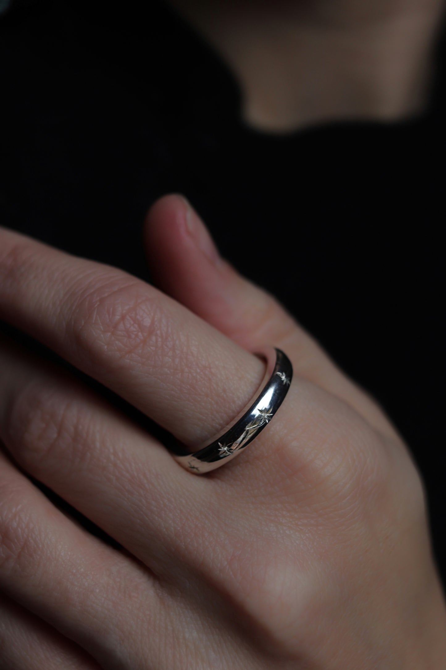 Close-up of a hand wearing a silver ring with a dark background