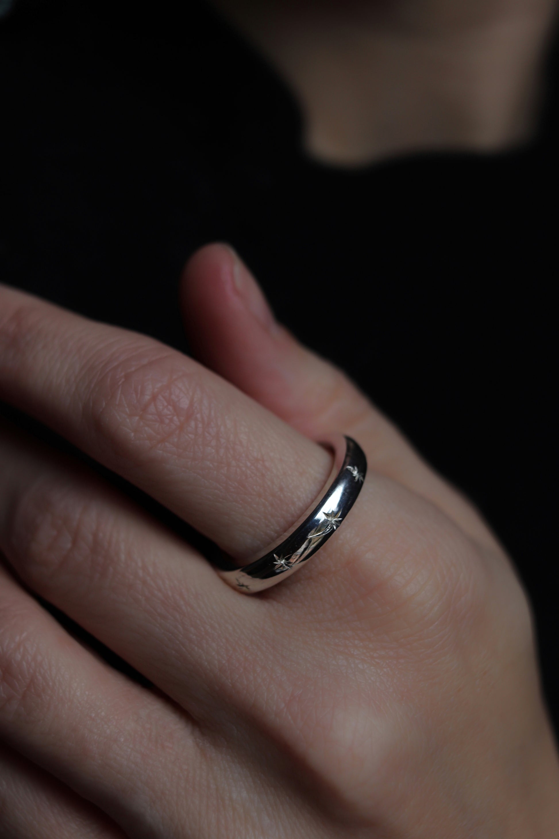 Close-up of a hand wearing a silver ring with a dark background