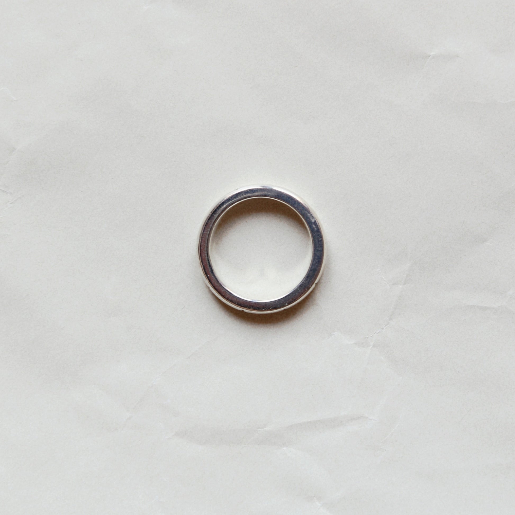 A simple silver-toned metal ring band photographed from above on a wrinkled off-white paper background.