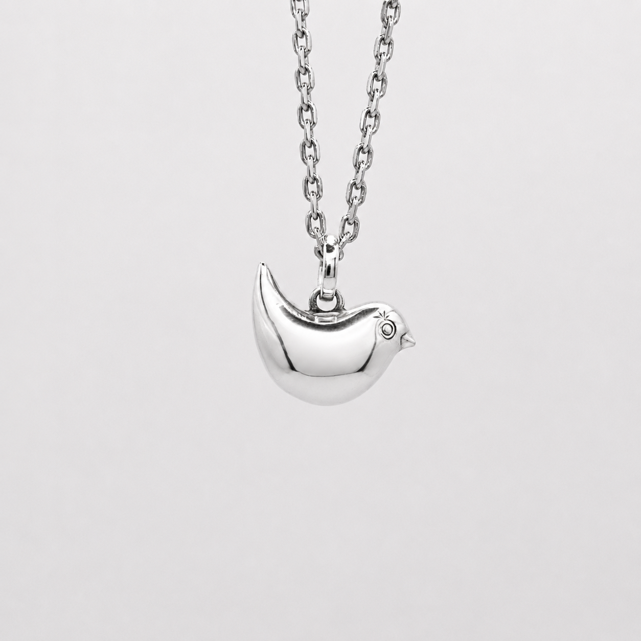 Silver necklace with a bird pendant on a light gray background