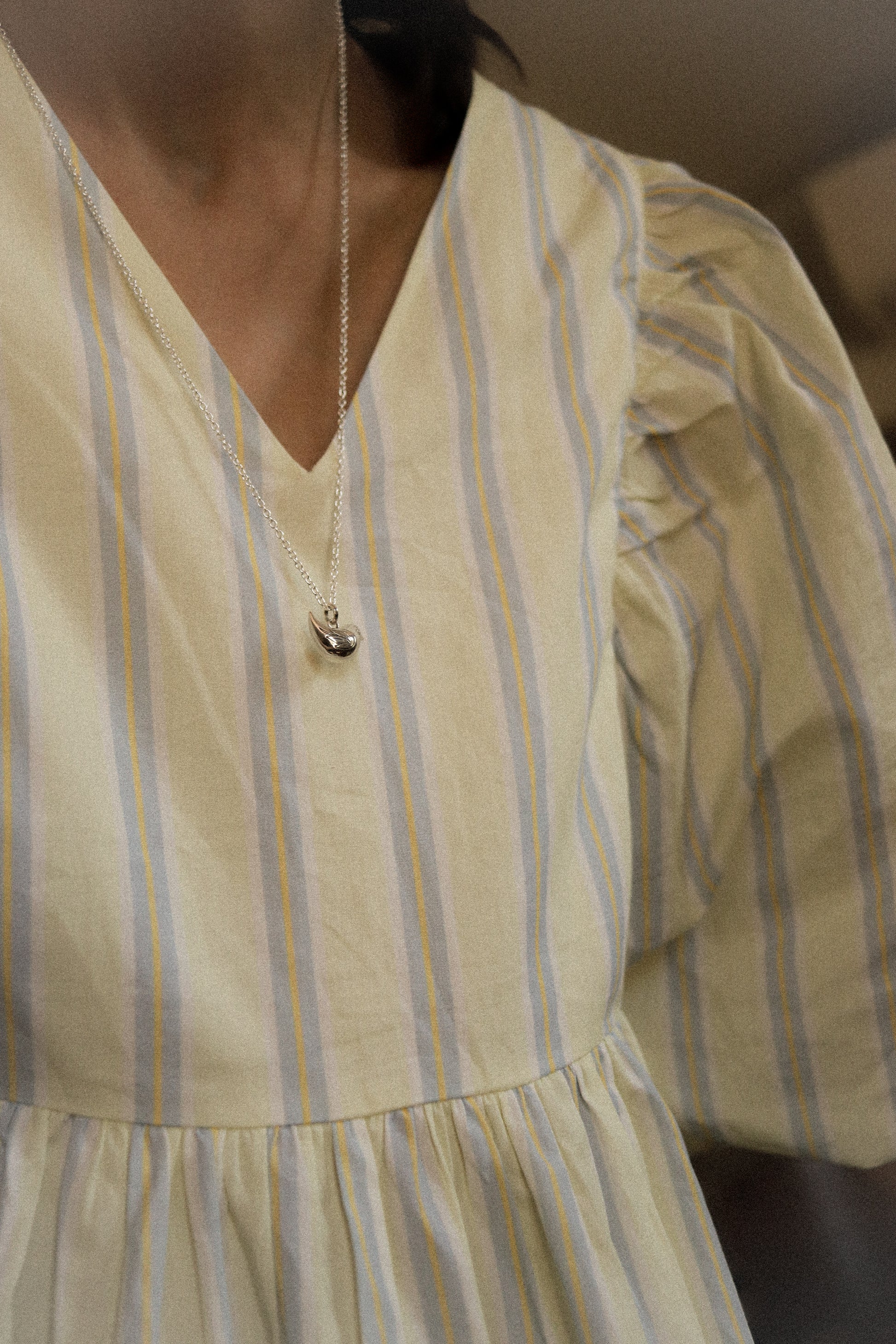 Close-up of a person wearing a yellow and blue striped dress with a necklace.