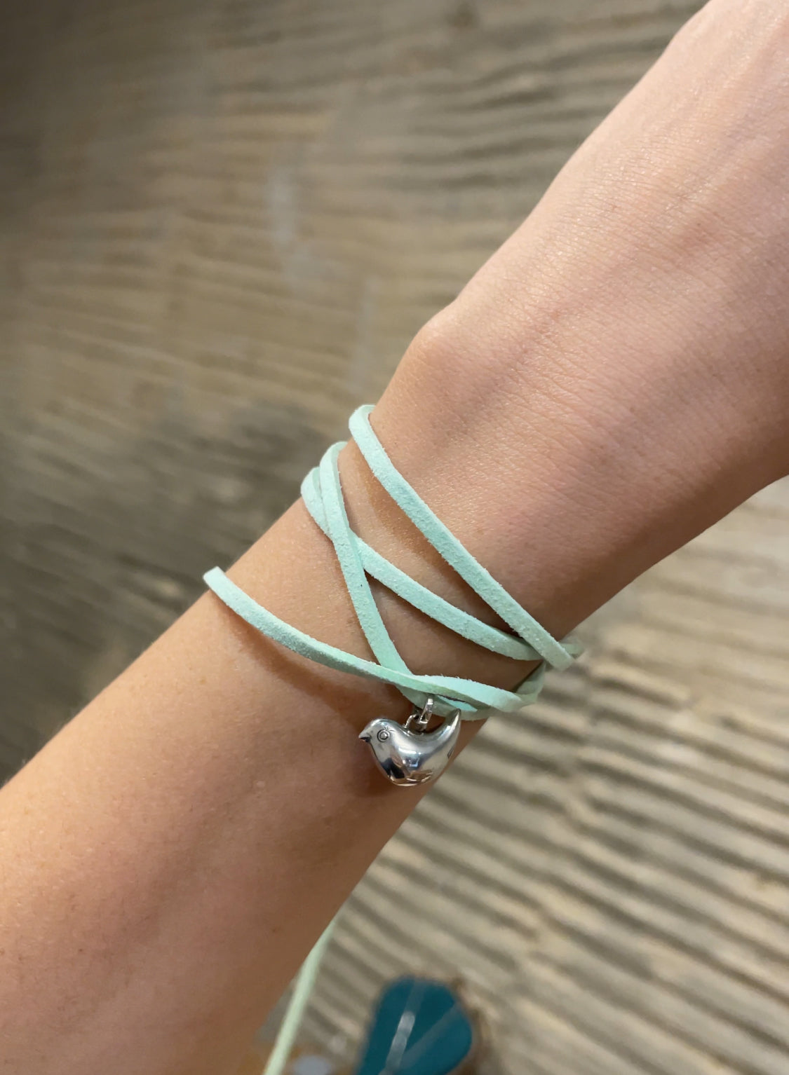 Light blue bracelet with a silver charm on a wrist against a neutral background