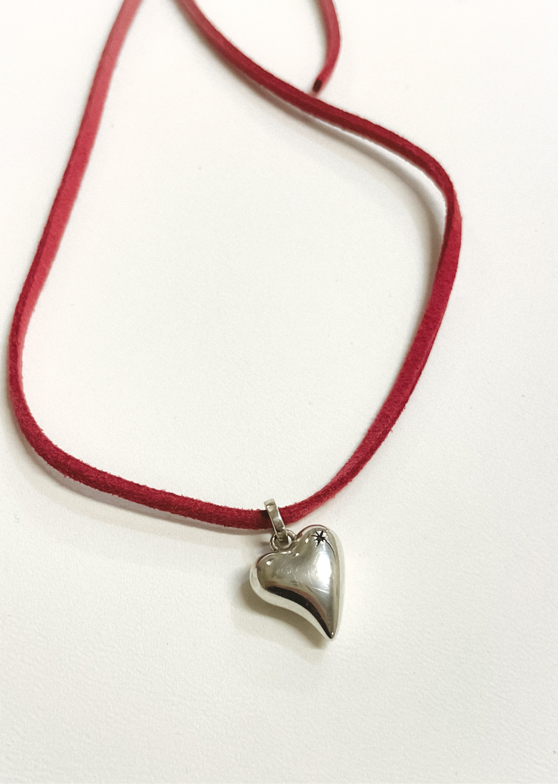 Necklace with a heart-shaped pendant on a red cord against a white background