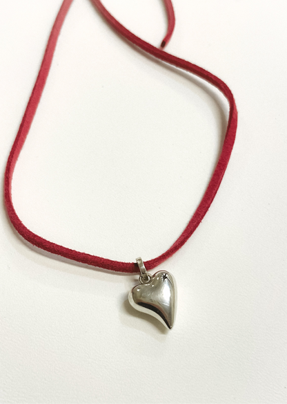 Necklace with a heart-shaped pendant on a red cord against a white background