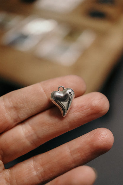 Silver heart-shaped charm held between fingers with a blurred background