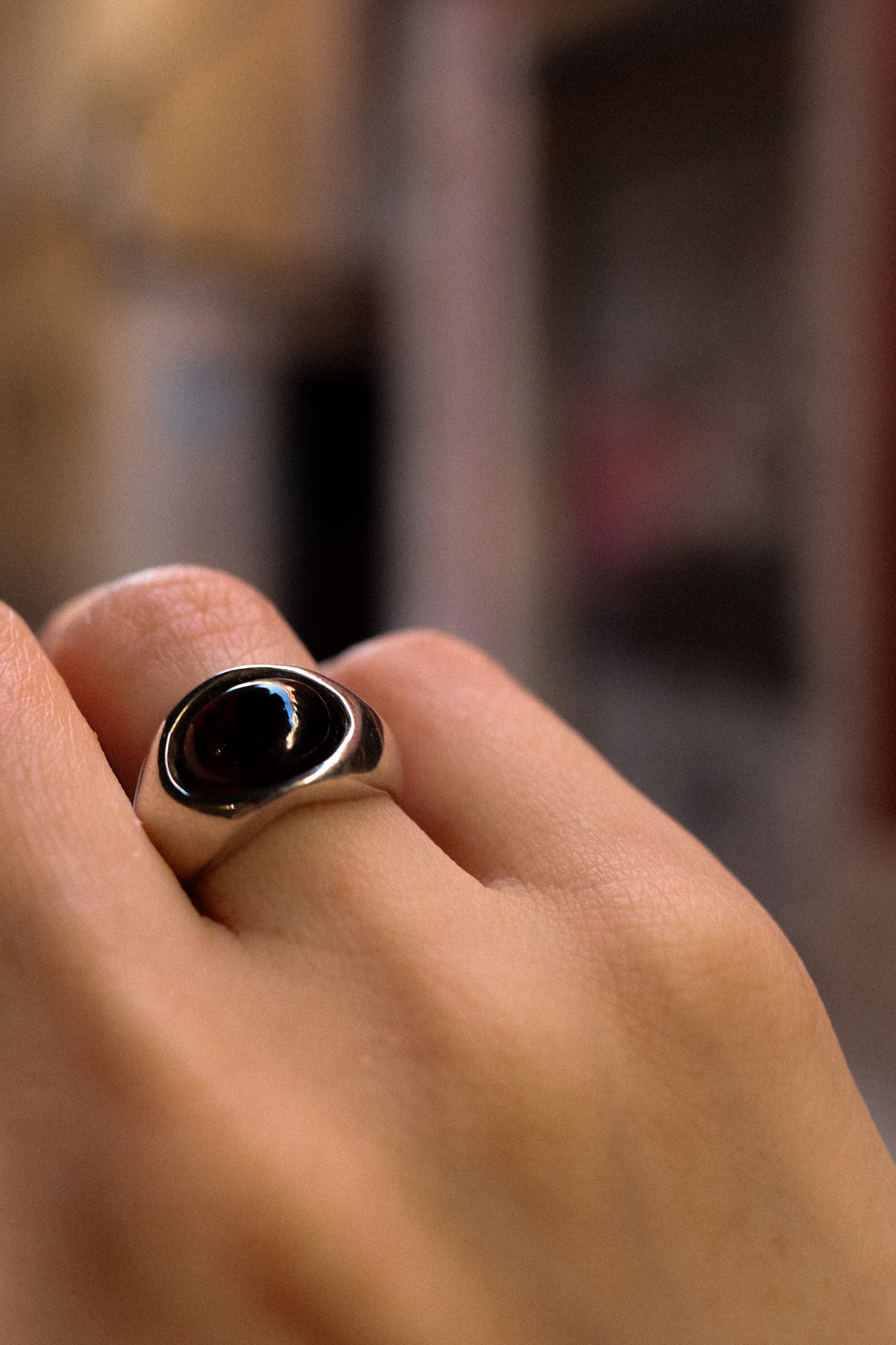 Close-up of a hand wearing a ring with a black stone on a blurred background
