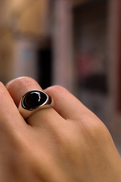 Close-up of a hand wearing a ring with a black stone on a blurred background