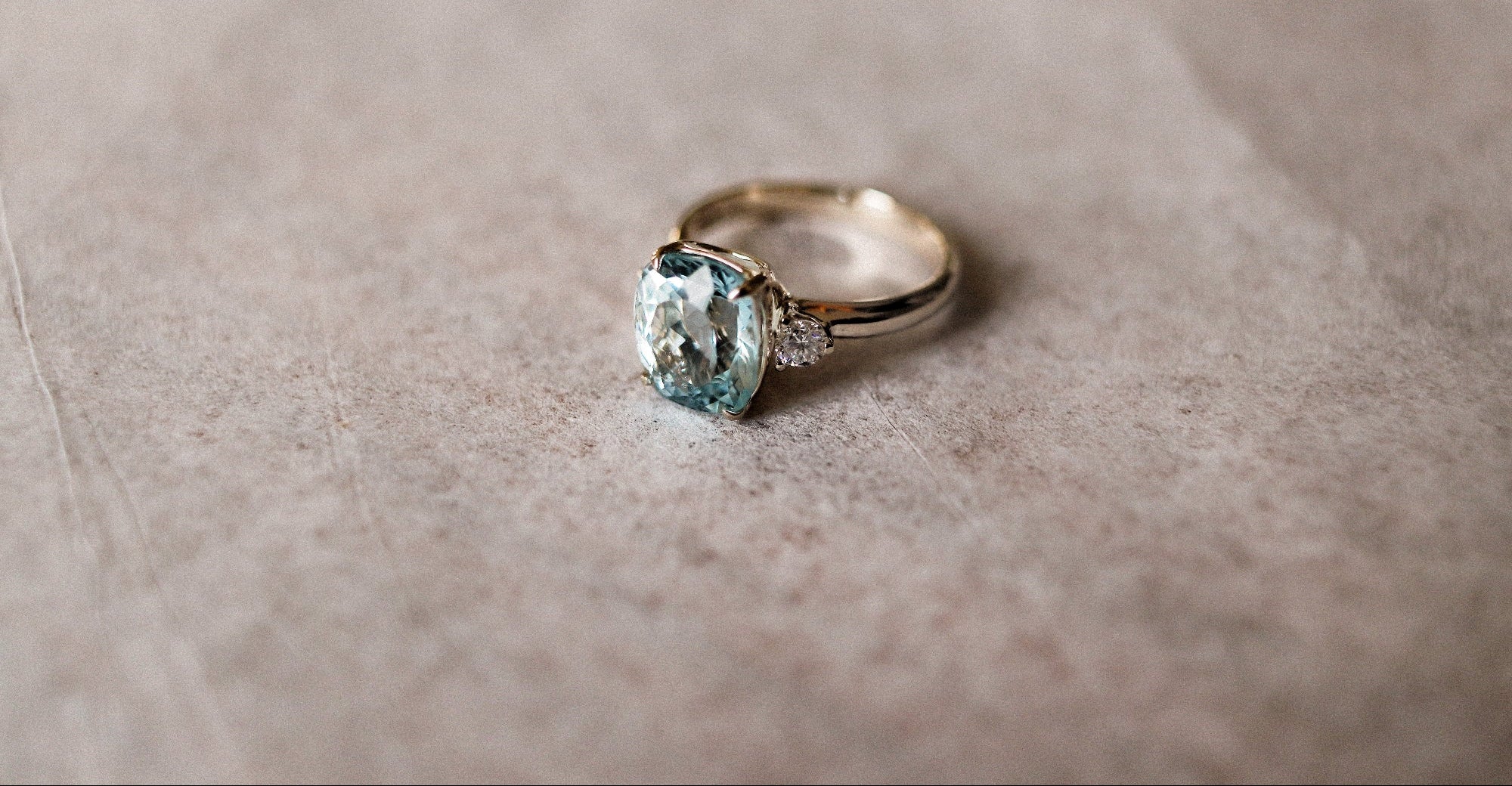 White gold ring with a blue aquamarine gemstone on a beige fabric background