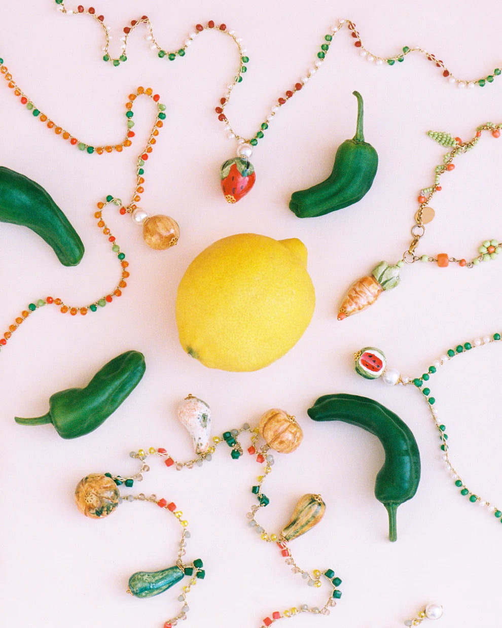 Colorful beaded necklaces with green peppers and a lemon on a white background