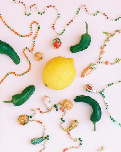 Colorful beaded necklaces with green peppers and a lemon on a white background