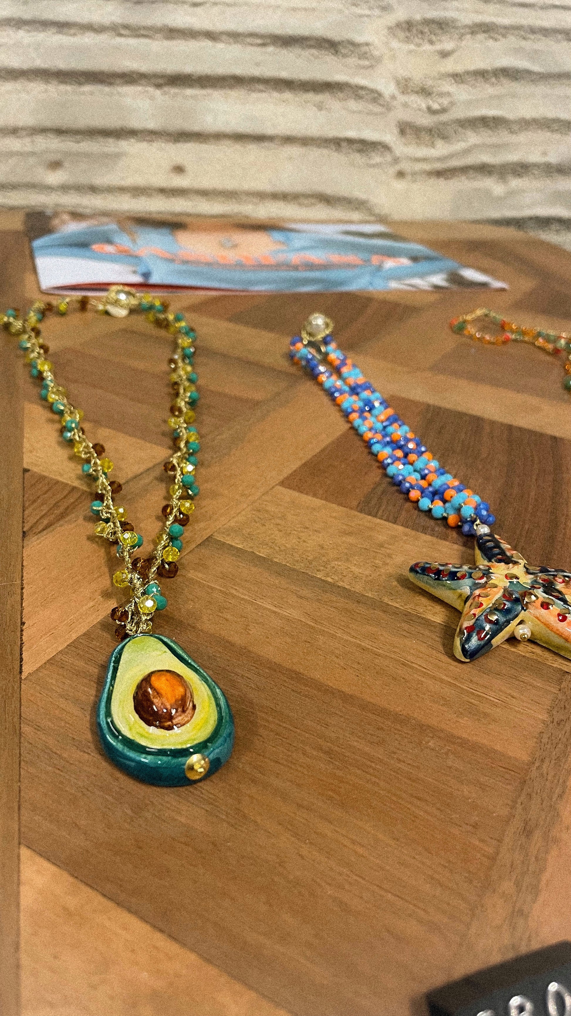 Necklace with avocado pendant and colorful bracelet on a wooden surface