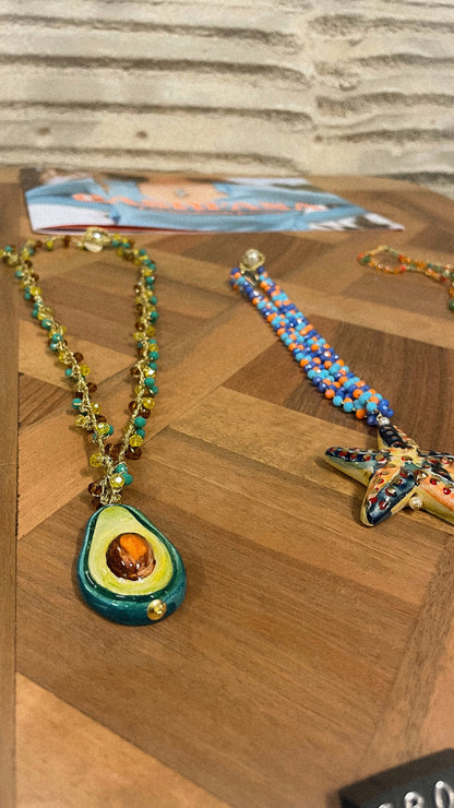 Necklace with avocado pendant and colorful bracelet on a wooden surface