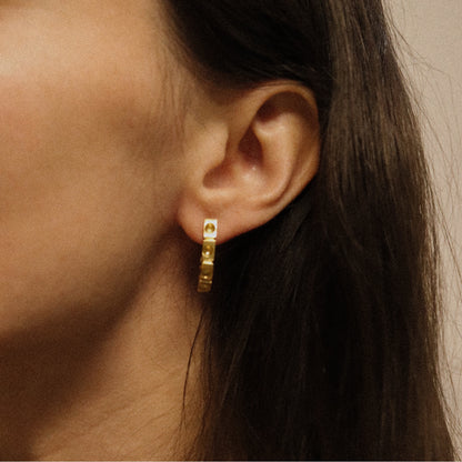 Gold hoop earrings worn by a person with dark hair.