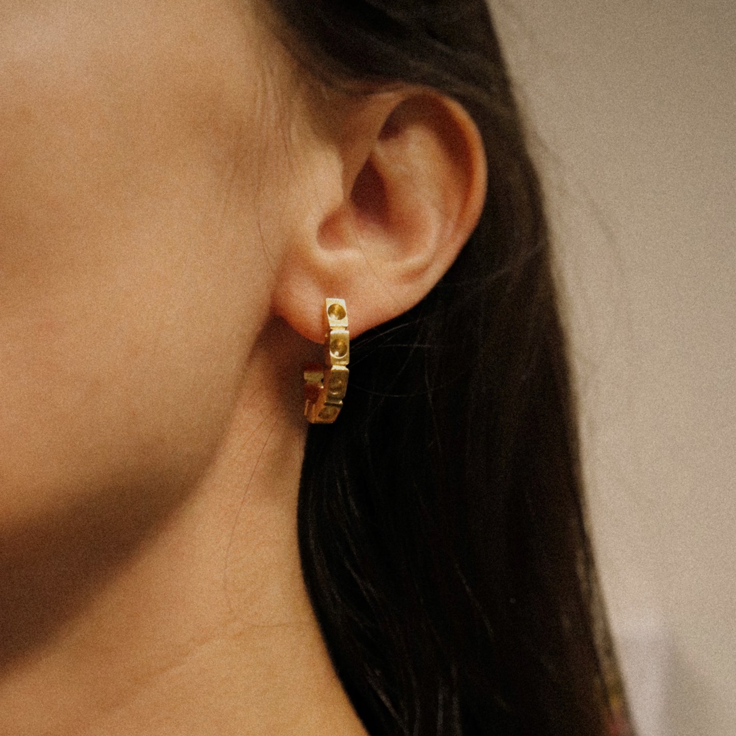 Close-up of a person wearing a gold hoop earring with a blurred background