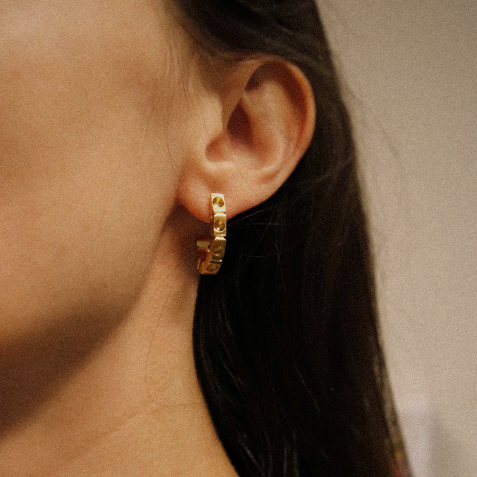 Close-up of a person wearing a gold hoop earring with a blurred background